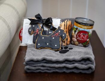 Stack of towels with a paw print, dog-shaped cookies, and a can of Purina ONE dog food on a wooden surface.