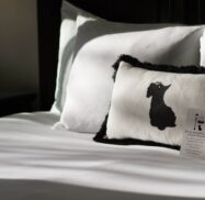 A bed with white sheets and a pillow featuring a silhouette of a dog. A note card is placed on the bed.