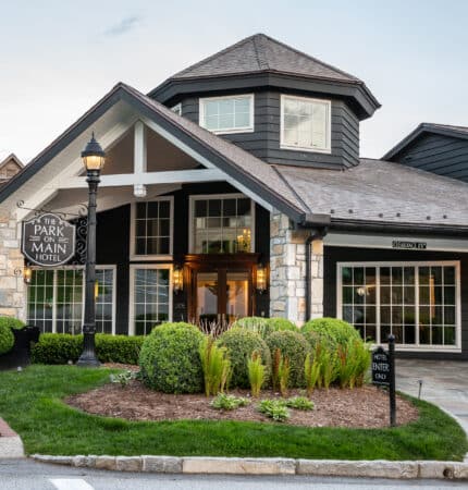 A charming hotel entrance with a rustic, modern design featuring a stone and wood facade, landscaped greenery, and a "Park on Main Hotel" sign.