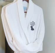 White bathrobe with "The Park on Main" logo hanging on a wooden hanger in a closet.