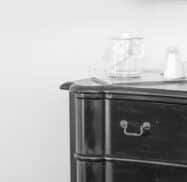 Black and white image of a wooden dresser with a curved handle. On top are a clear plastic cup with a lid and another lid without a cup.
