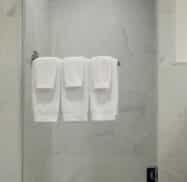 A glass shower with white marble tiles and three folded white towels hanging on a rail.