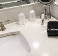 Bathroom countertop with a sink, two wrapped cups, a small bottle, and a black towel labeled "makeup" next to a tabletop mirror.