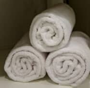 Three neatly rolled white towels are stacked on a shelf.