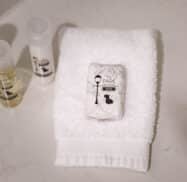 White towel with a wrapped soap bar and three small bottles of toiletries on a bathroom countertop.