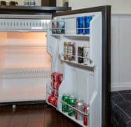 Open mini fridge with assorted drinks on the door shelves, including soda and canned beverages, and empty shelves inside.