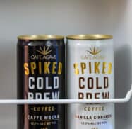 Two cans of Cafe Agave Spiked Cold Brew, one Caffe Mocha and one Vanilla Cinnamon, each with 12.5% alcohol by volume, are placed on a shelf.