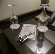 A hotel room desk with two upside-down wine glasses, a corkscrew, a telephone, and a menu labeled "libations.