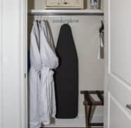 Closet with robes, ironing board, iron, safe, and luggage rack.