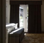 A dimly lit room with a large window covered by dark curtains, a white piano, a gray bench, and a patterned rug on the floor.