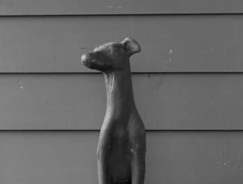 A statue of a seated dog in a minimalist style graces the lobby of a dog-friendly hotel in Highlands, NC, set against a paneled wall. Black and white image.