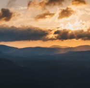 Sunrise over misty mountain ranges with clouds partially covering the sky.