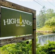 A wooden sign reads "Highlands Elev. 4118" next to a waterfall surrounded by dense greenery under a clear sky.