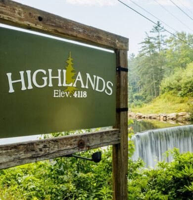 A wooden sign reads "Highlands Elev. 4118" next to a waterfall surrounded by dense greenery under a clear sky.