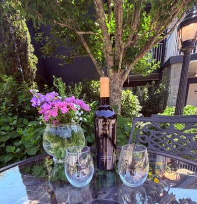 Serene hotel garden patio with wine, flowers, and lush greenery under a sunny sky.